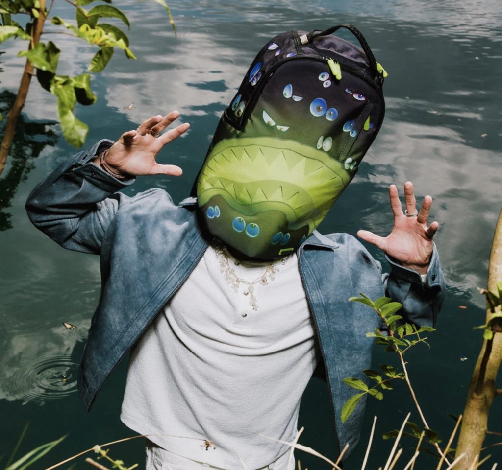 background water swamp scene, a person wearing SPRAYGROUND Eyes All A Glow DLXR Backpack glowing in the dark with signature shark mouth and luminous eye graphics